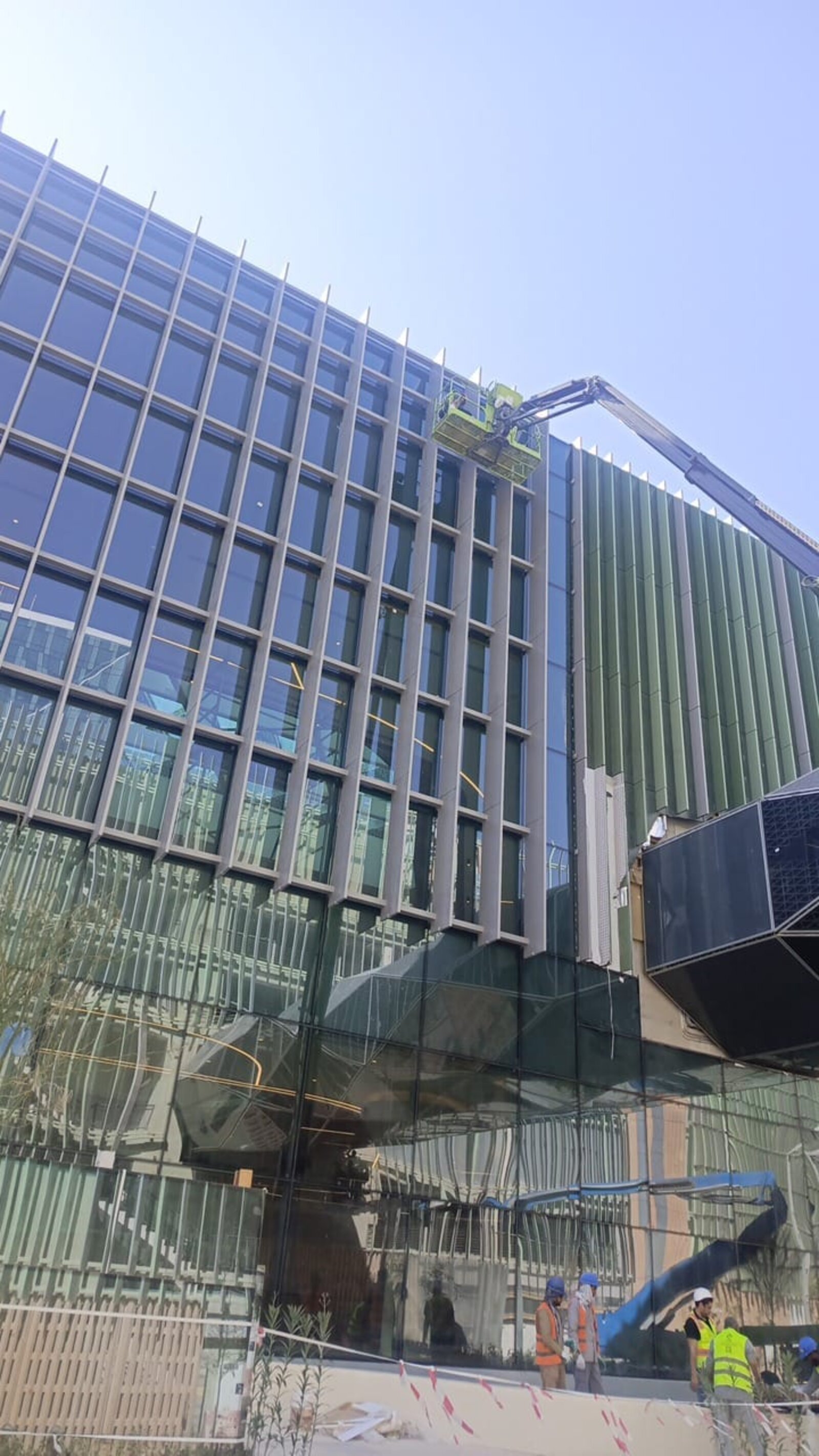 فريق شركة تنظيف واجهات بالرياض ينظف واجهة زجاجية وكلادينج أخضر لمبنى حديث بحي العارض باستخدام رافعة - حلول وتميز