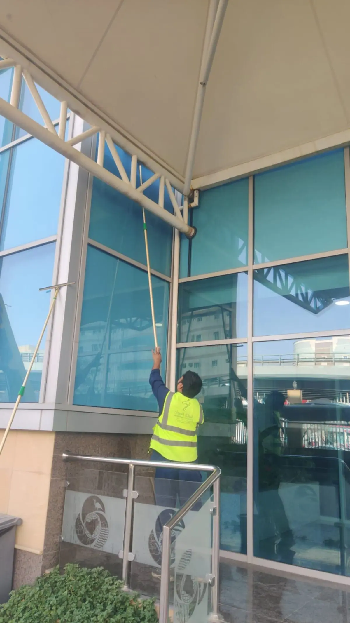 عامل من شركة تنظيف واجهات مدارس وفنادق بالرياض ينظف واجهة زجاجية لمدخل فندق أو مدرسة