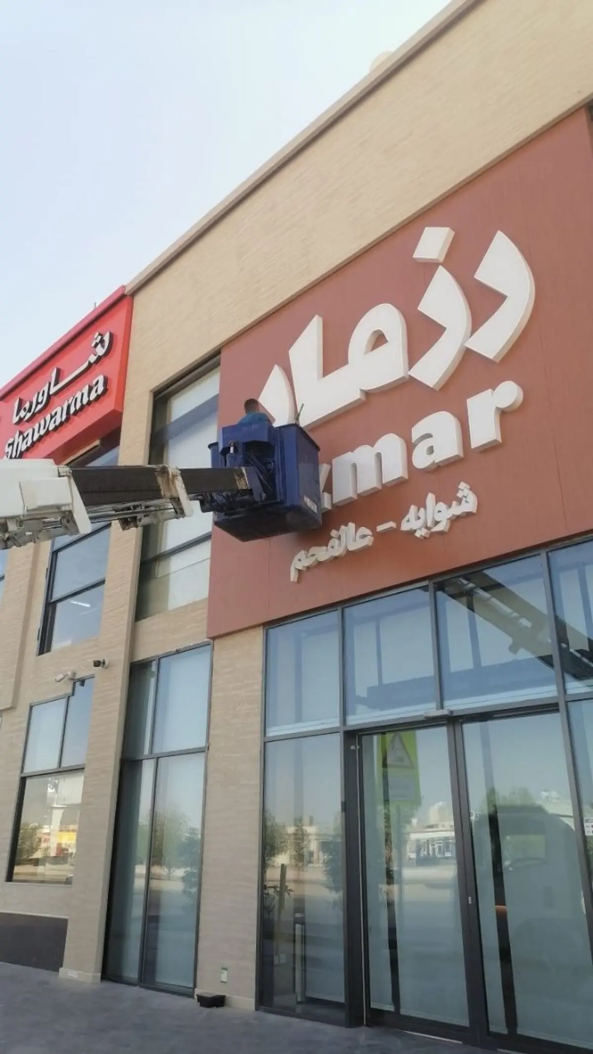 عامل من شركة تنظيف واجهات بالرياض ينظف لافتة محل تجاري مرتفعة باستخدام رافعة متحركة