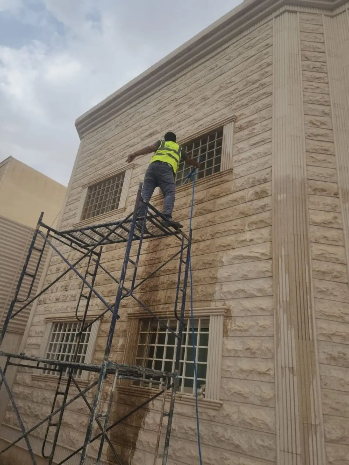 عامل من شركة تنظيف بيوت وفلل بالرياض ينظف واجهة فيلا حجرية على ارتفاع باستخدام برج سقالة