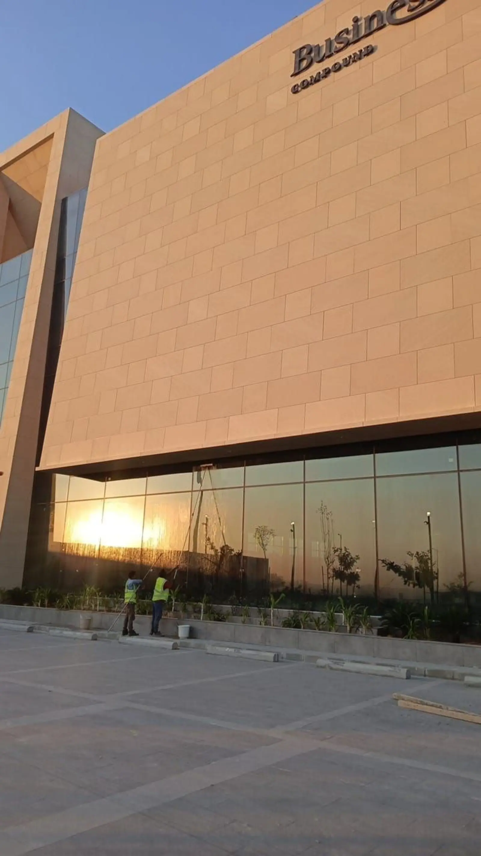 فريق شركة تنظيف جدران واسوار بالرياض ينظف واجهة زجاجية لمبنى تجاري بحي الياسمين وقت الغروب - حلول وتميز